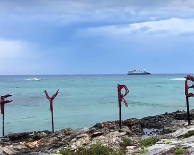 Ocean view with "FYRE" spelled out in sticks on rocky shore; distant boat visible under cloudy sky.