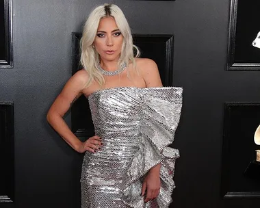 Lady Gaga in a silver sequined dress at the Oscars 2019, posing on the red carpet.