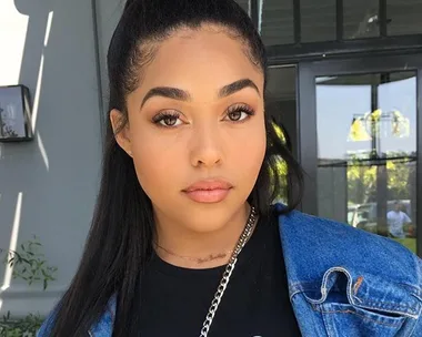 Young woman in denim jacket with long black hair tied back, standing outdoors, looking directly at the camera.