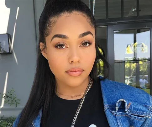 Young woman in denim jacket with long black hair tied back, standing outdoors, looking directly at the camera.