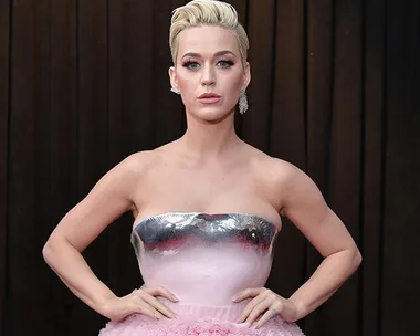 A person wearing a pink and silver strapless dress poses confidently with a short hairstyle and earrings.