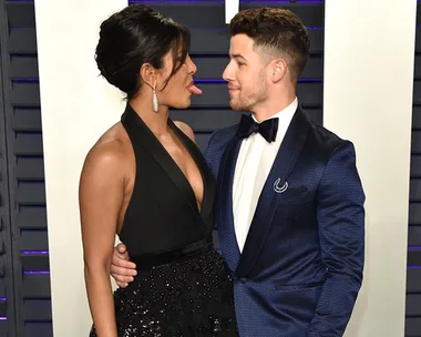 A woman in a black dress playfully sticks out her tongue at a man in a blue suit at a formal event.