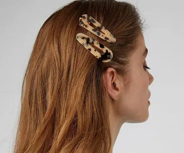 Woman with two tortoiseshell hair clips in side-parted brown hair, facing sideways against a light background.