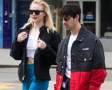 Two people walking on a city street, both wearing sunglasses and casual jackets.