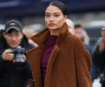 A person in a brown textured coat with photographers in the background.