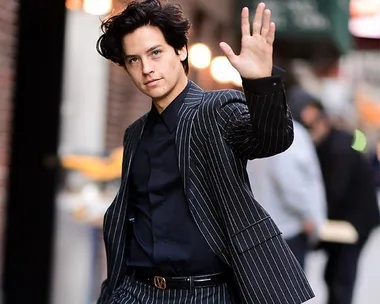 A person in a pinstripe suit waving on a city street.