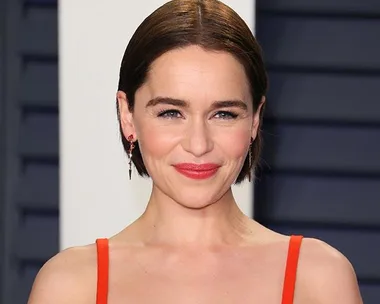 Actress in orange dress smiling at a formal event with a neutral background.