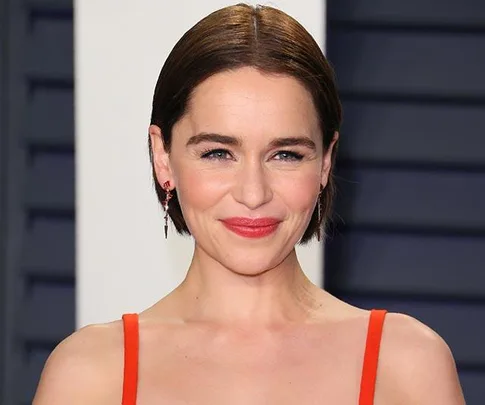 Actress in orange dress smiling at a formal event with a neutral background.