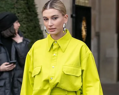 A woman in a neon green outfit with hoop earrings, standing outdoors in front of a building.