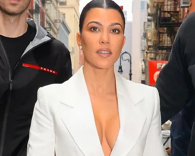 A woman in a white blazer walking down a city street with two people beside her.