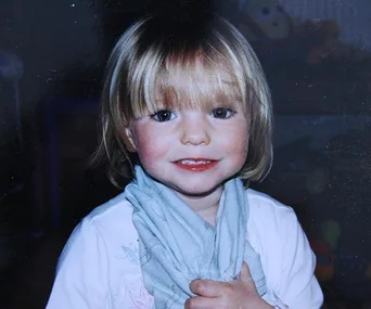 Young child with short blonde hair smiling, wearing a light blue scarf and white shirt.