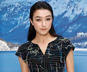 Woman in multicolored outfit stands in front of a snowy mountain backdrop.