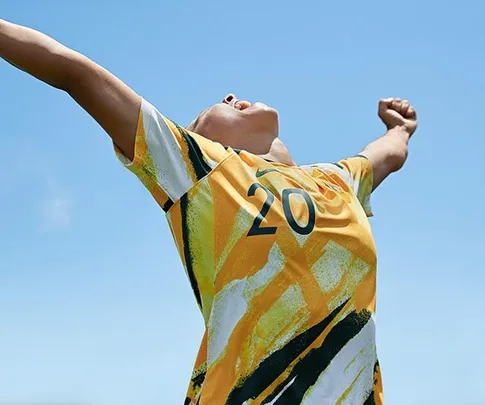 Soccer player in yellow-green jersey with number 20, arms raised triumphantly, under clear blue sky.