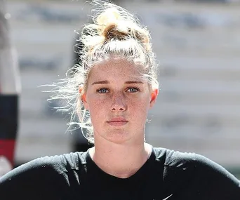 Woman with blonde hair tied up, wearing a black shirt, looking directly at the camera with a neutral expression.