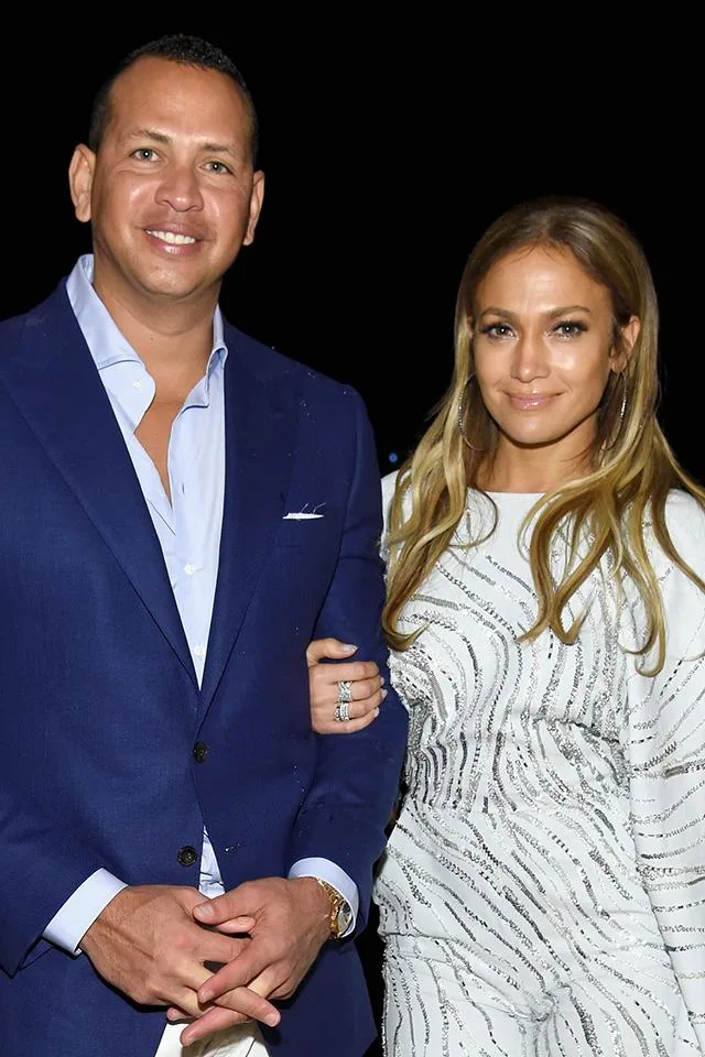 A man in a blue suit with a woman in a white patterned dress, smiling and standing close together.