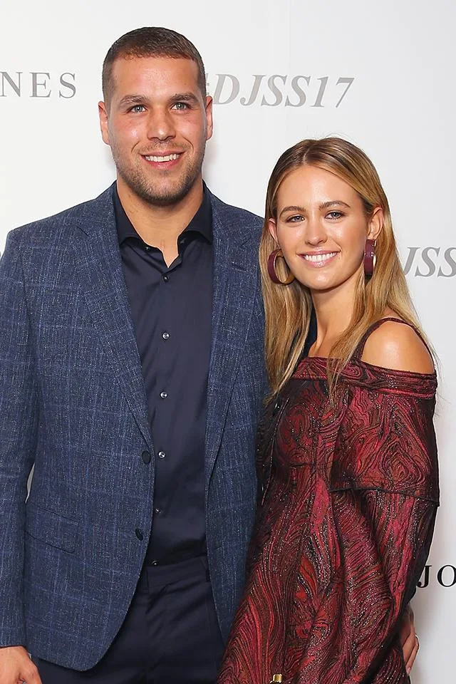 A man in a blue suit and a woman in a red dress smiling together at an event backdrop.