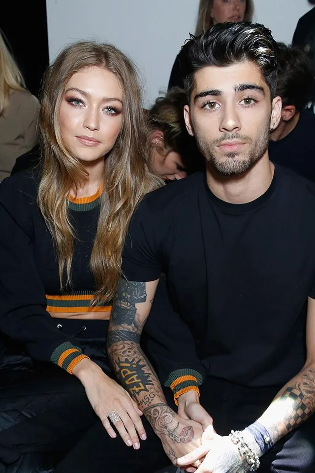 Two people sitting close, wearing black outfits, with one displaying tattooed arms.