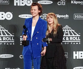 Harry Styles in a blue suit holding a trophy with Stevie Nicks in a black outfit at the Rock & Roll Hall of Fame event.