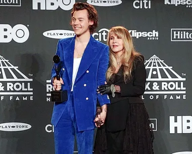 Harry Styles in a blue suit holding a trophy with Stevie Nicks in a black outfit at the Rock & Roll Hall of Fame event.