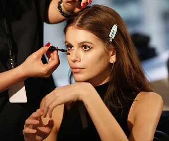 Person getting mascara applied with a makeup brush, hair clipped back, and wearing a black top.