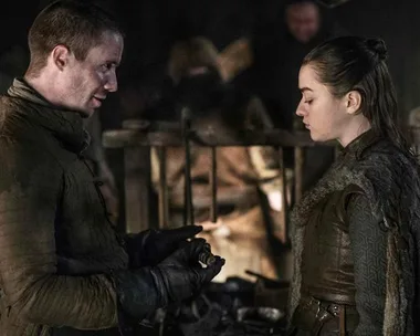 Gendry and Arya stand together in a dimly lit room, discussing something important in "Game of Thrones."