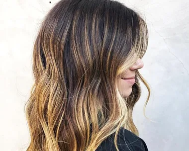 Woman with long, wavy hair featuring balayage highlights blending from dark brown to blonde.