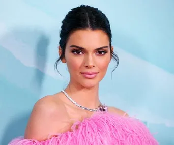 A woman in a pink feathered outfit poses in front of a blue background.