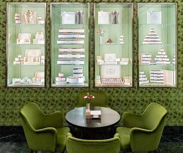 Display shelves with assorted luxury products, green chairs around a table with flowers in a well-lit elegant shop.