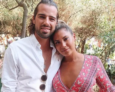 Man and woman embracing outdoors, smiling. Man in white shirt, woman in red patterned dress.