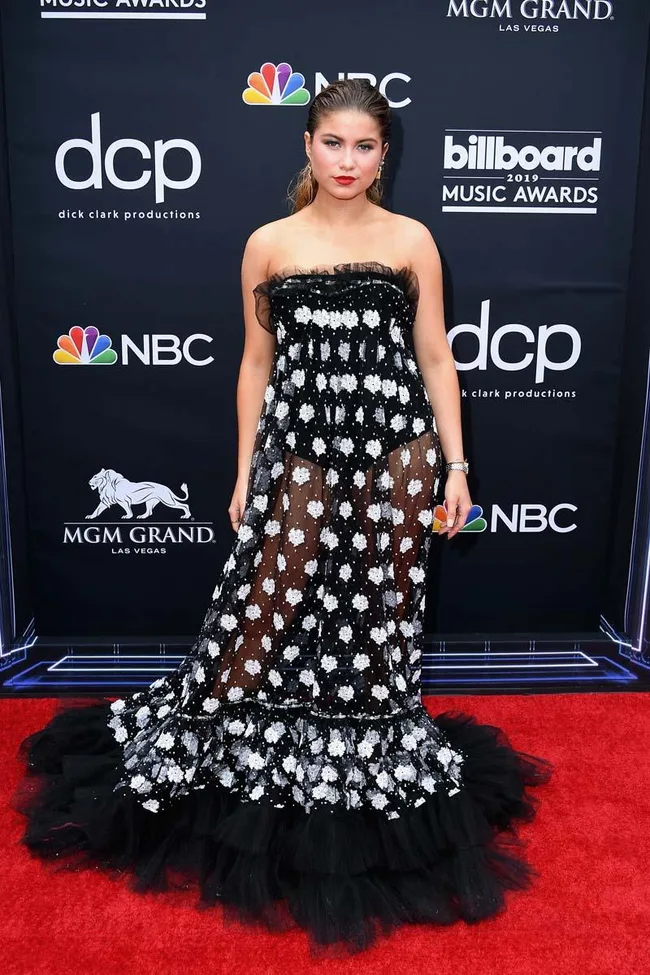 Young woman in a sheer black dress with white floral patterns at the 2019 Billboard Music Awards red carpet.