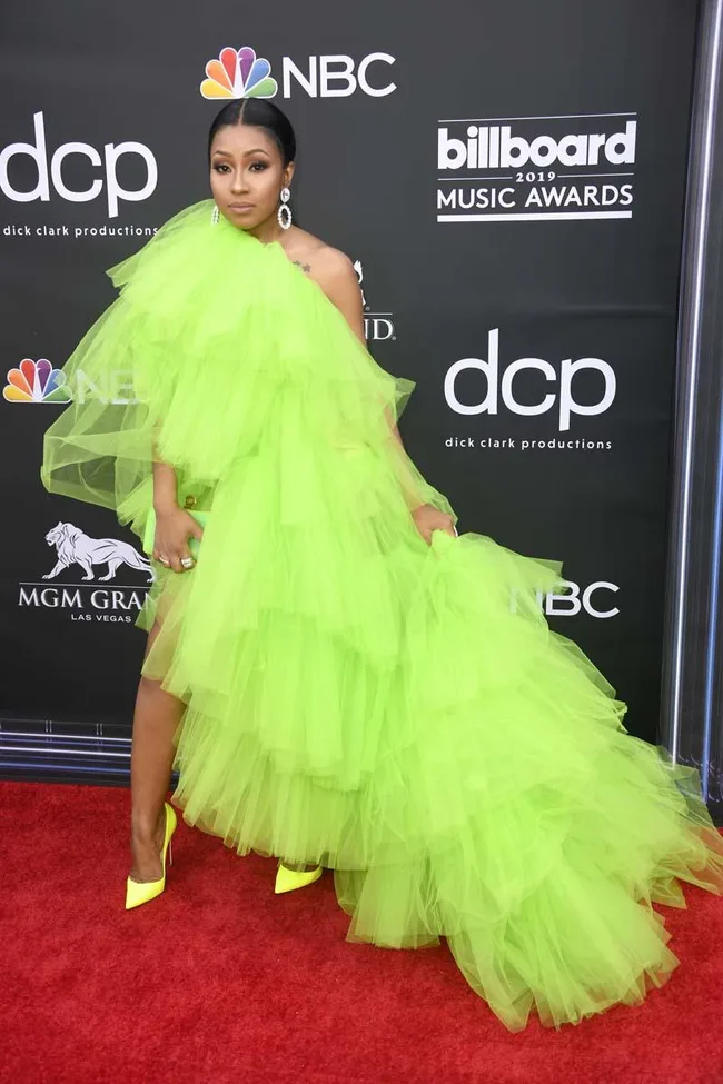 A person in a bright green tulle gown and yellow heels on the red carpet at the 2019 Billboard Music Awards.