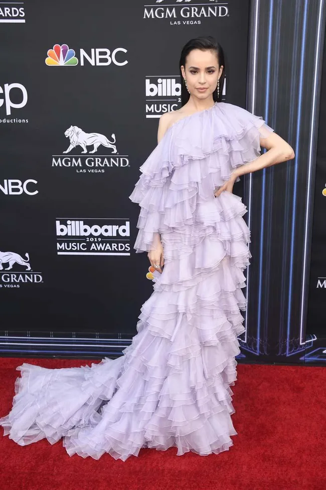 Person in a layered lavender gown on the Billboard Music Awards red carpet, posing with one hand on hip.