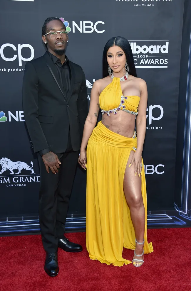A man in a black suit and a woman in a yellow dress on the red carpet at the Billboard Music Awards.