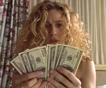 Woman with curly hair holds several $100 bills, looking surprised.