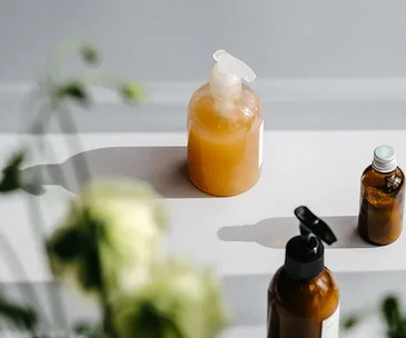 Bottles of eco-friendly skincare products on a sunlit surface with blurred flowers in the foreground.