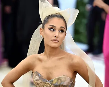 A person in a strapless gown with a large bow in their hair, looking to the side at a formal event.