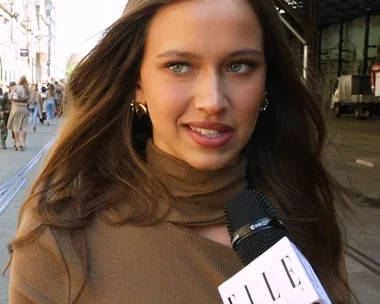 Young woman with long hair in a brown turtleneck being interviewed by Elle magazine outdoors.