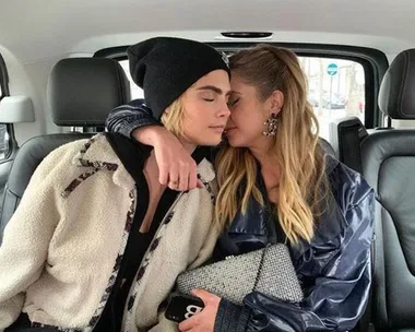 Two people sitting closely together in a car, one wearing a beanie, the other holding a glittery clutch.