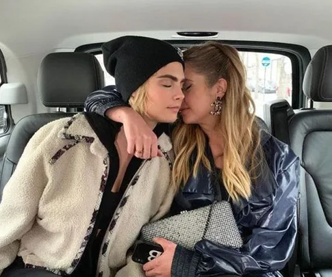 Two people sitting closely together in a car, one wearing a beanie, the other holding a glittery clutch.