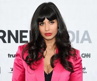 A person with long hair in a bright pink blazer poses confidently against a backdrop with text.