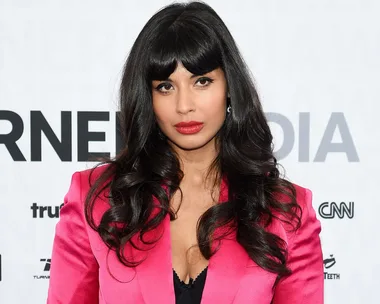 A person with long hair in a bright pink blazer poses confidently against a backdrop with text.