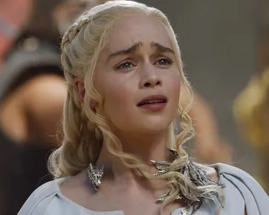 Daenerys Targaryen looking concerned, with braided hair and a detailed necklace in "Game of Thrones" scene.