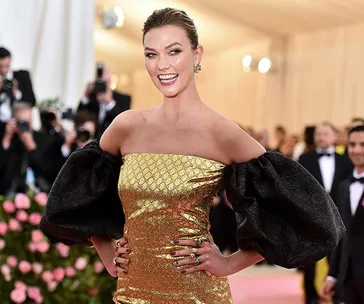 A person at the Met Gala 2019 wearing an off-shoulder golden dress with large black sleeves, smiling for the cameras.