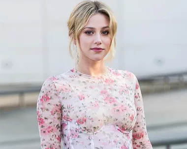 A person in a floral dress poses outdoors against a neutral background.