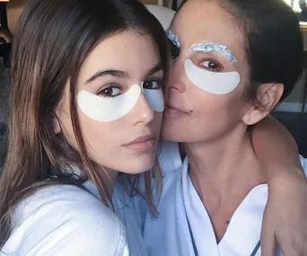 Two women wearing under-eye patches and robes, close together, showcasing a skincare routine.