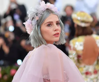 Woman with blue hair and floral crown in pink dress at a formal event.