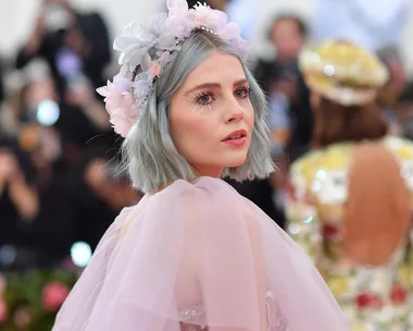 Woman with blue hair and floral crown in pink dress at a formal event.