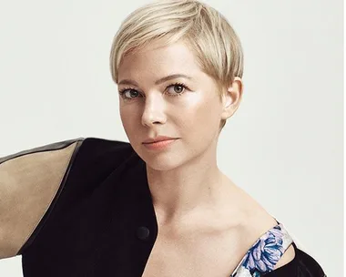 A woman with short blonde hair wearing a stylish black and floral outfit poses against a plain background.