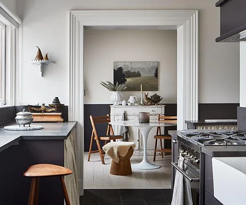 Modern kitchen with vintage decor, featuring a dining table, wooden chairs, and a landscape painting on the wall.