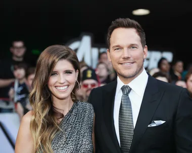 A smiling couple poses on the red carpet at a movie premiere, surrounded by other attendees.